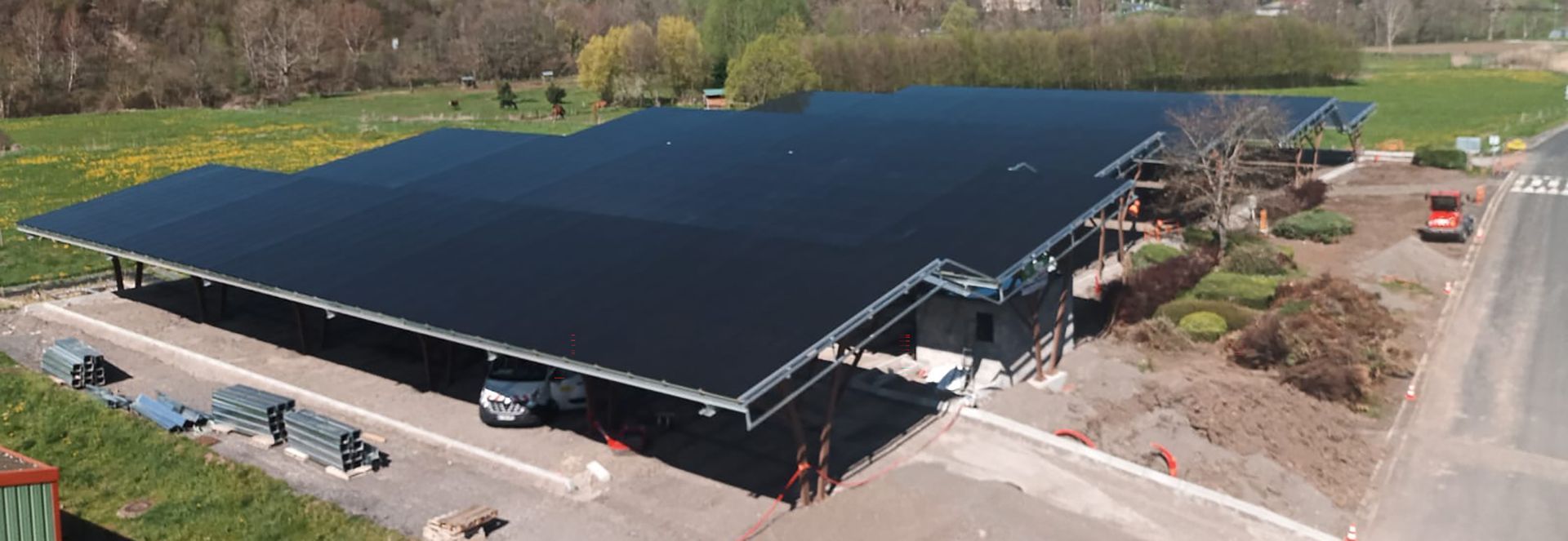 Grande structure de panneaux solaires au-dessus d'un parking, avec un bâtiment en arrière-plan.