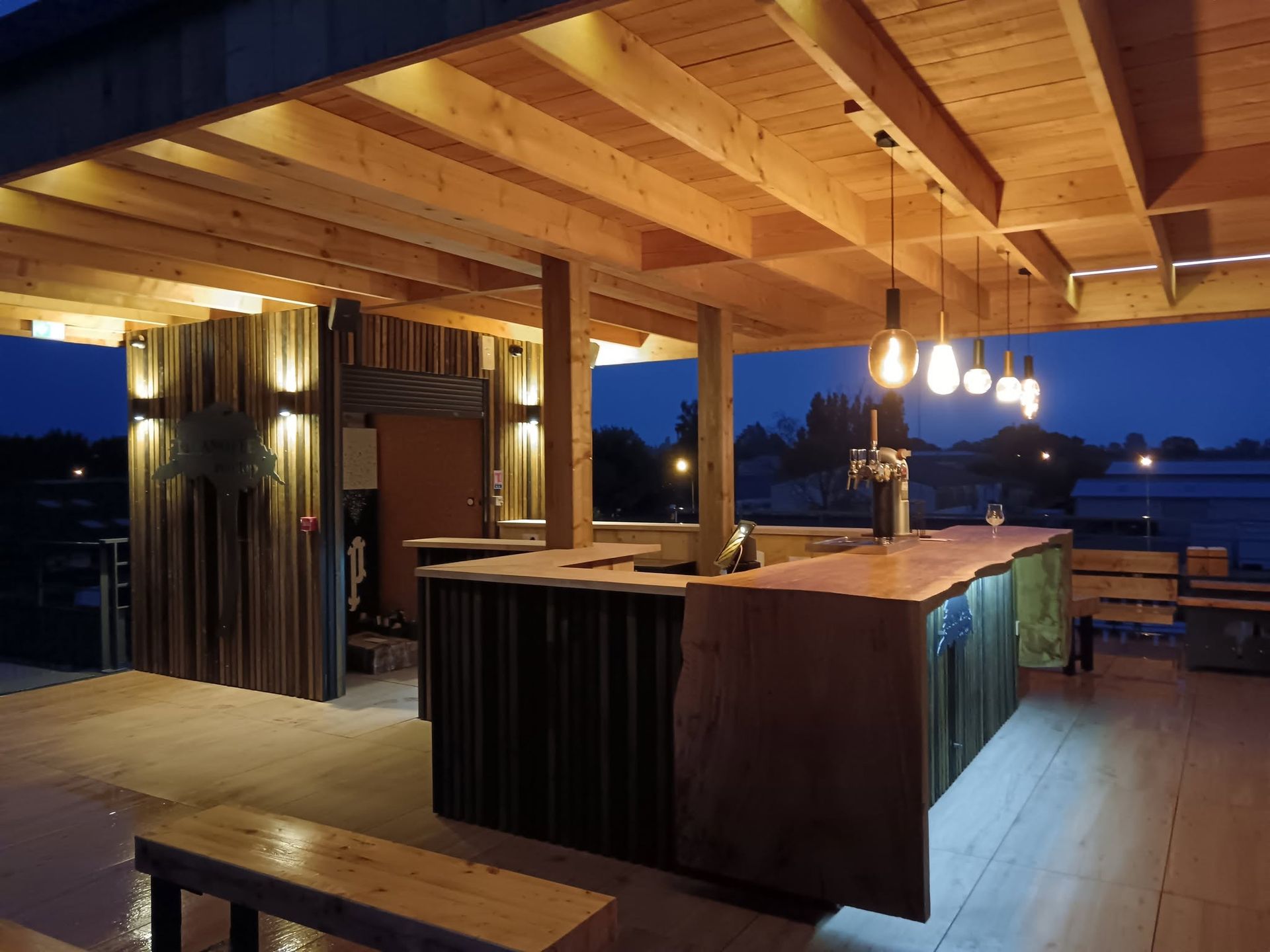 Un bar extérieur avec un comptoir en bois et des luminaires suspendus.