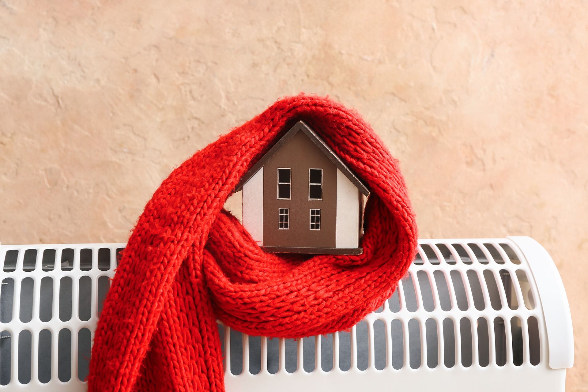 Écharpe rouge enroulée autour d’une petite maquette de maison posée sur un radiateur blanc.