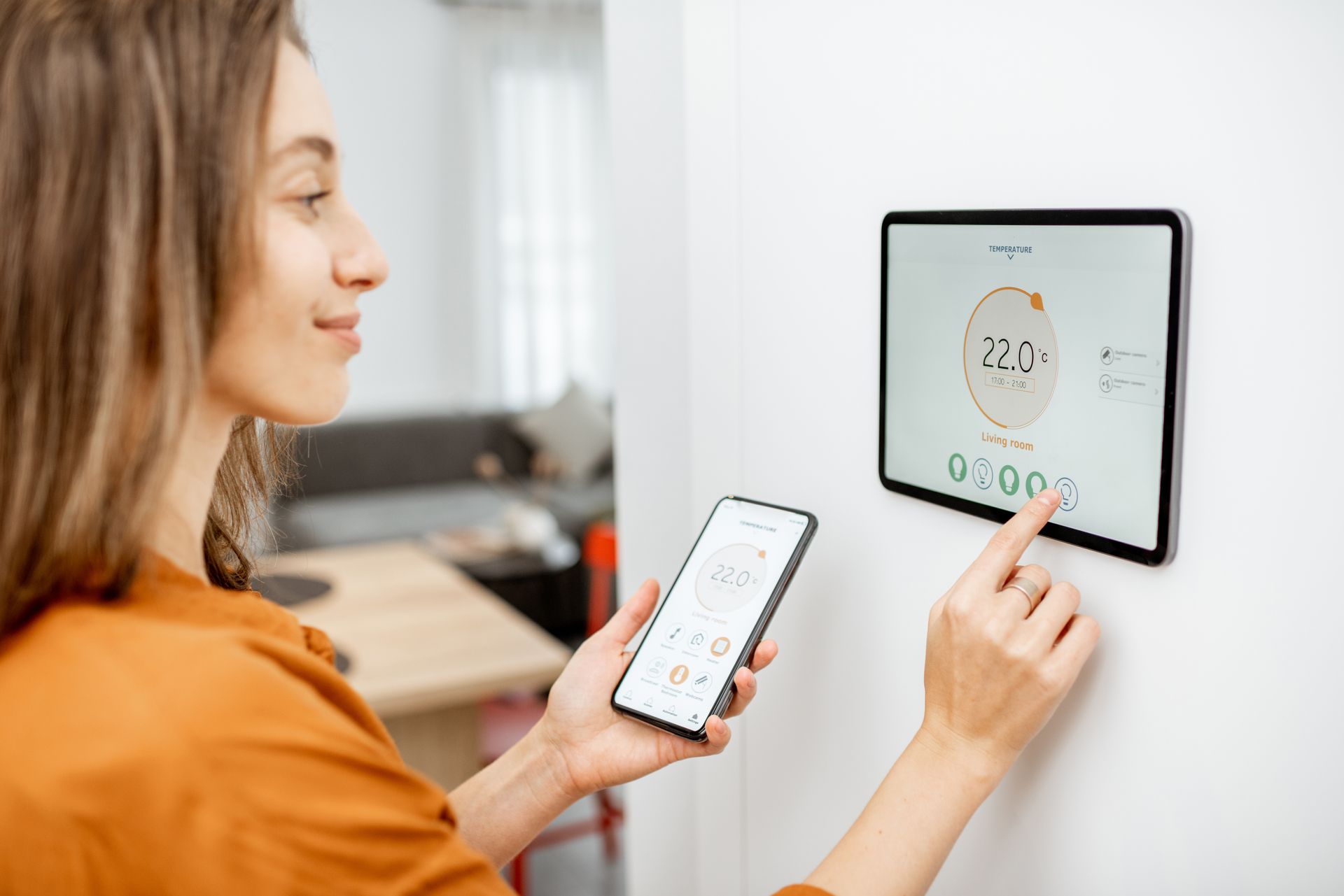 Une femme utilise un smartphone pour contrôler un thermostat connecté.