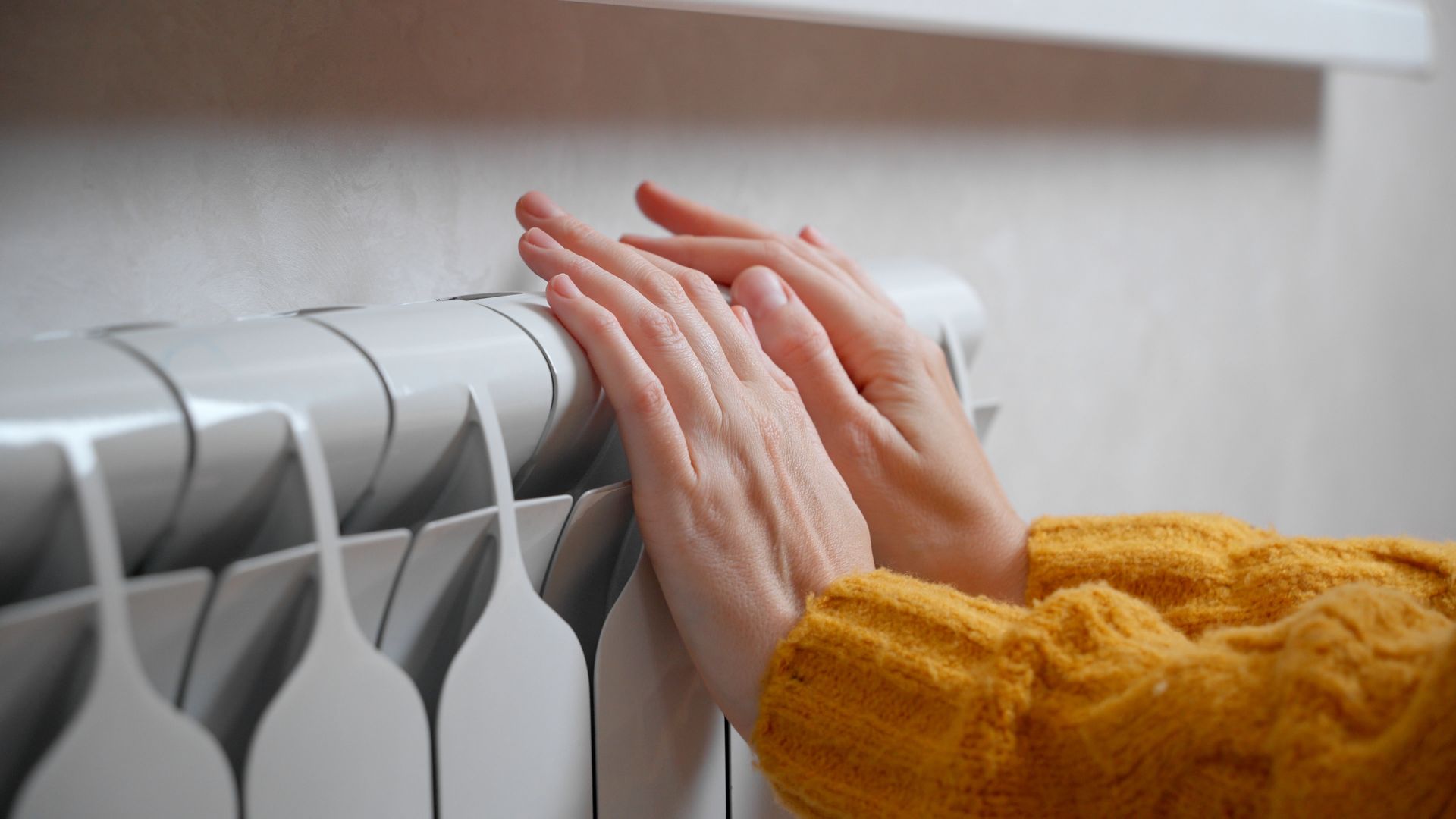 Des mains posées sur un radiateur blanc pour se réchauffer.