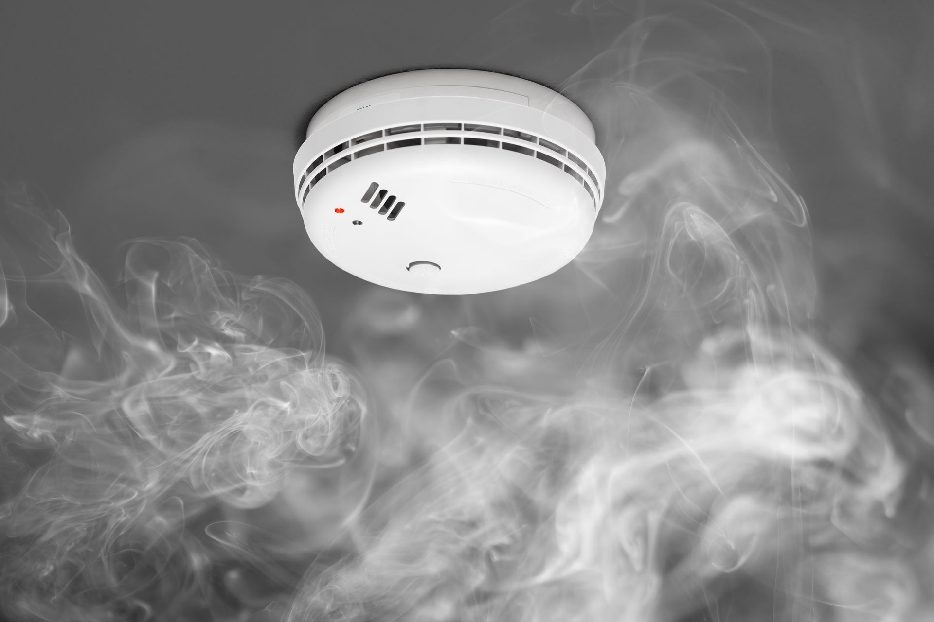 Détecteur de fumée blanc au plafond, dans un épais nuage de fumée.