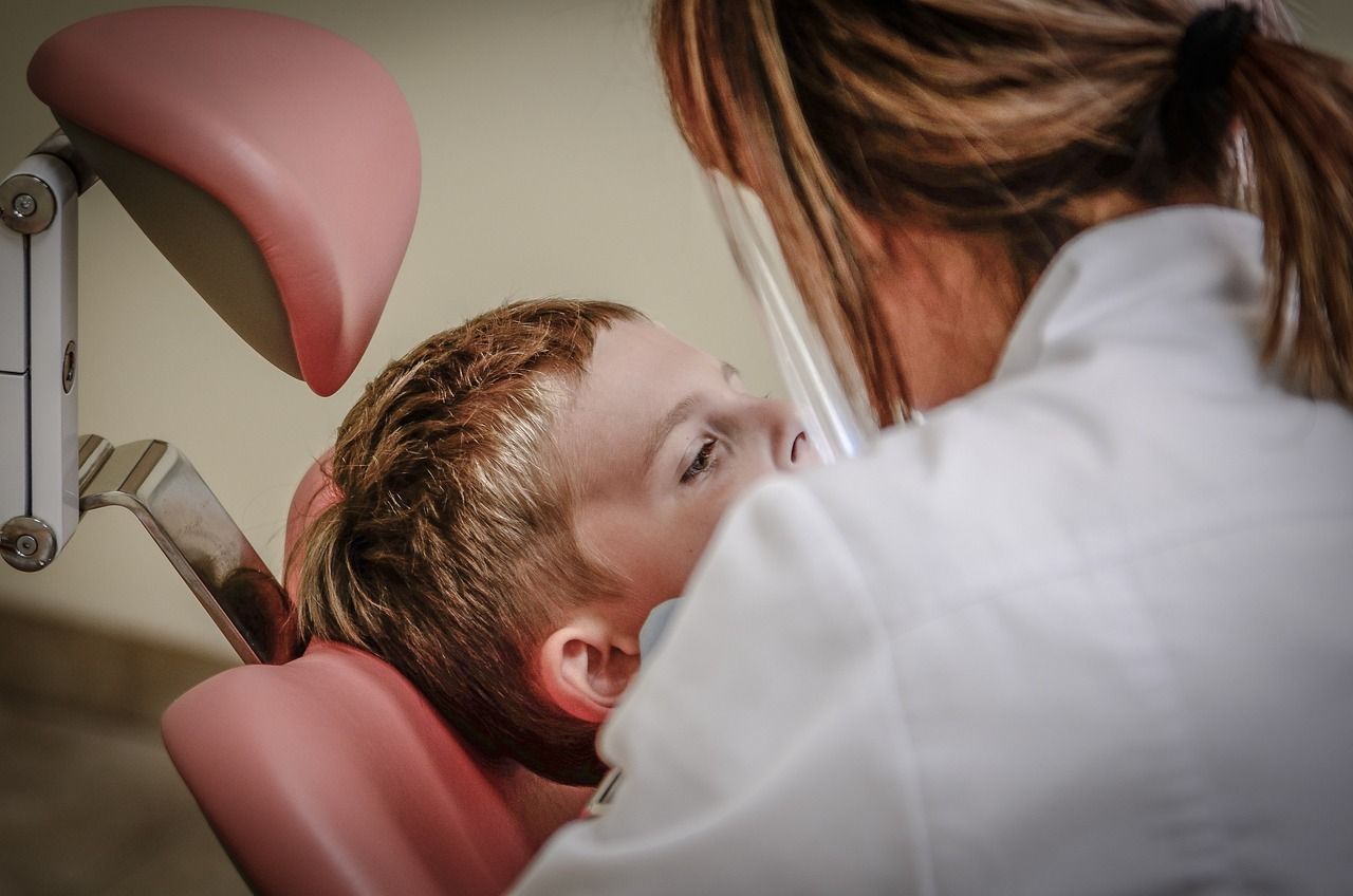 Kinderzahnarzt kümmert sich um ein Kind der im Zahnarztstuhl sitzt