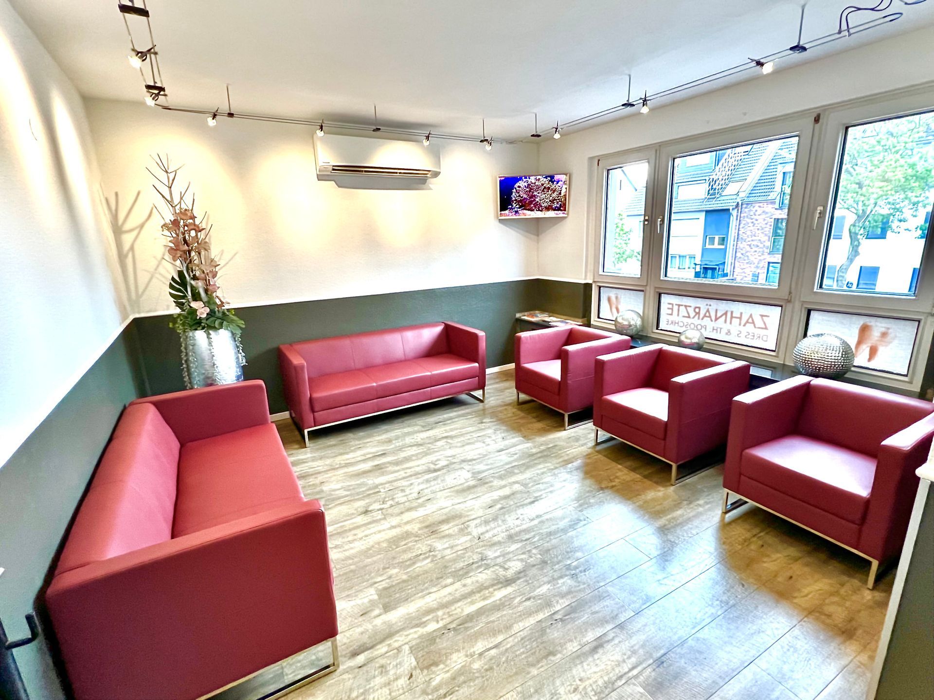 Helles Wartezimmer mit roten Sofas, grünen Wänden, Holzboden und großen Fenstern