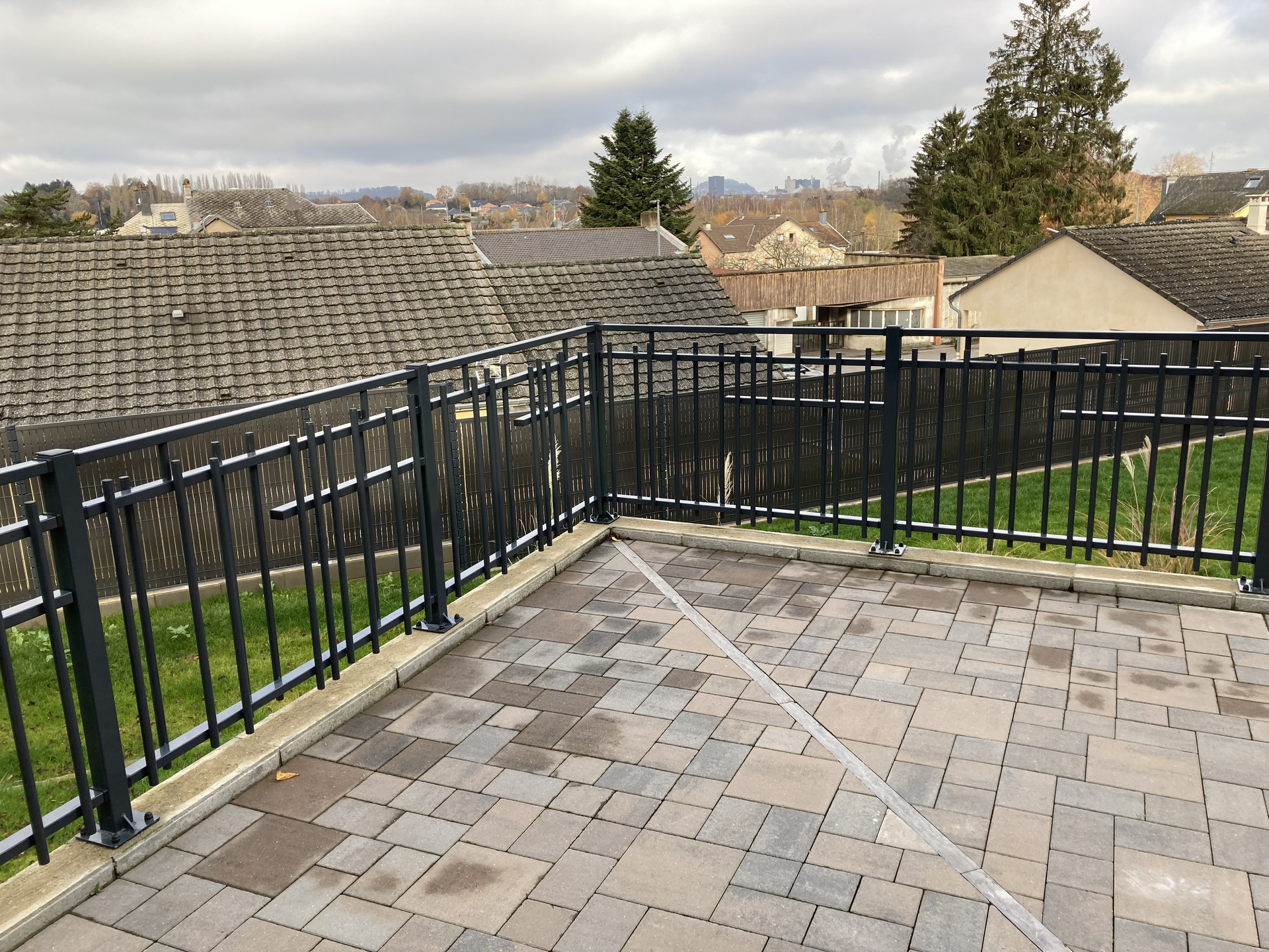 Terrasse avec une clôture en métal et une allée en briques