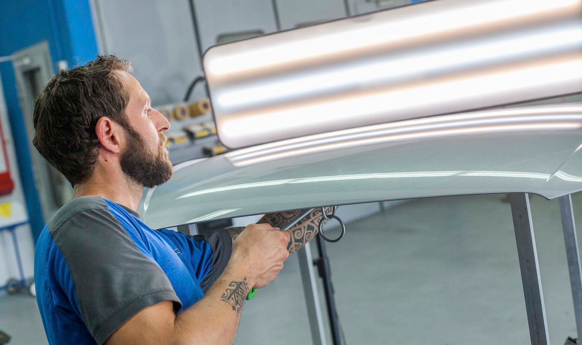 Ein Mann in einem blauen Hemd steht mit verschränkten Armen in einer Garage.