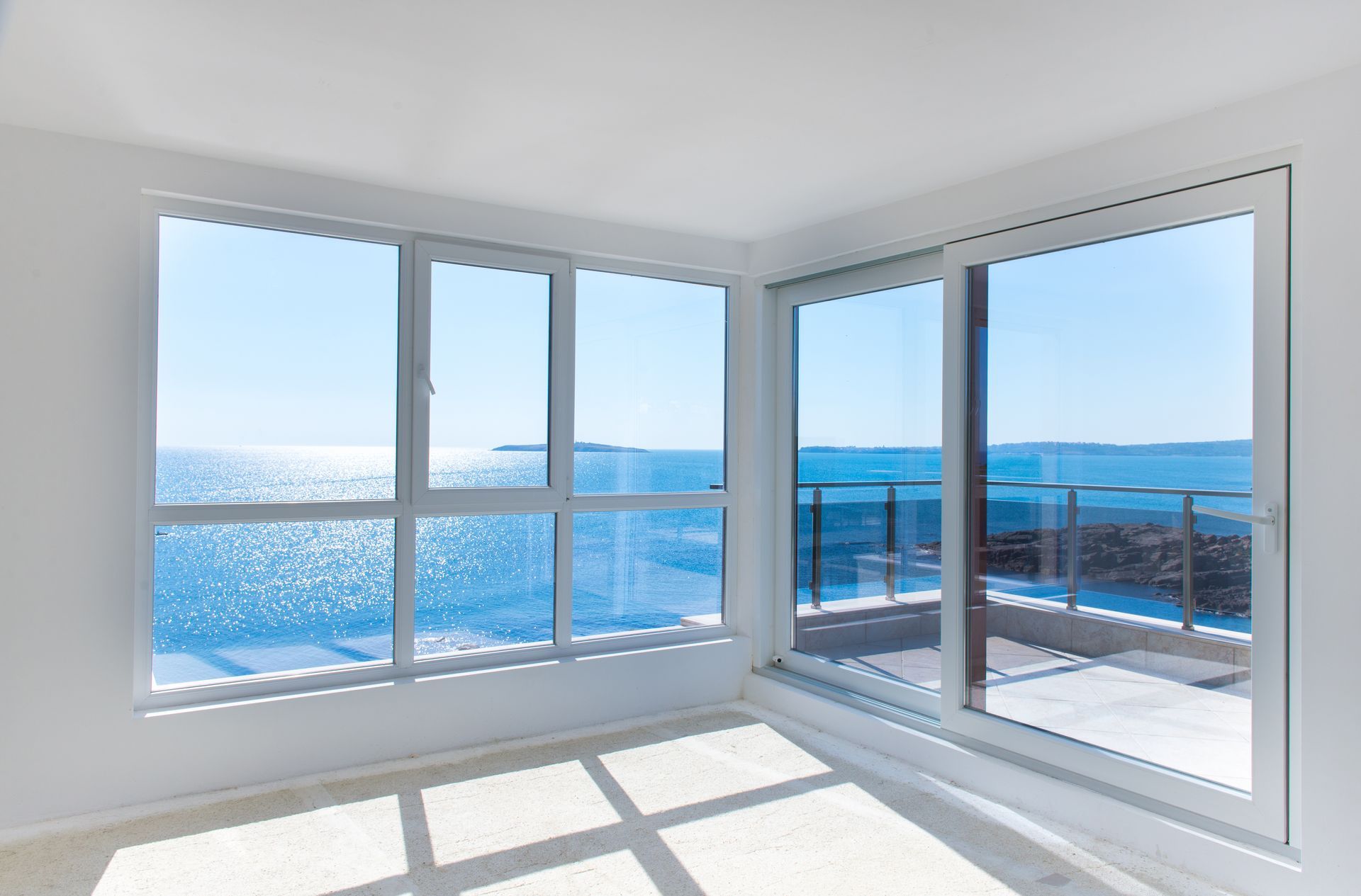 Habitación luminosa y vacía con grandes ventanales con vistas a un soleado océano.