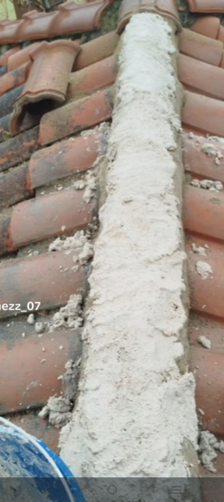 Sellado de mortero blanco agrietado que se extiende verticalmente entre tejas rojas.