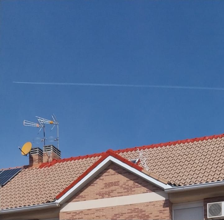 Azotea con tejas rojas, antena de televisión y panel solar bajo un cielo azul despejado.