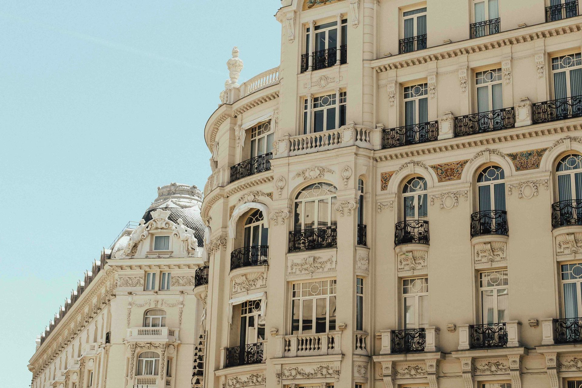Edificio histórico ornamentado de color crema con balcones contra un cielo azul claro