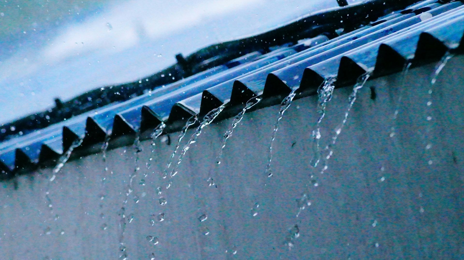 Goteo de lluvia desde el borde de un techo de metal azul con carámbanos o agua congelada colgando debajo.