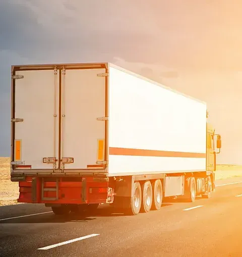 Camión semirremolque blanco circulando por una autopista con luz solar.
