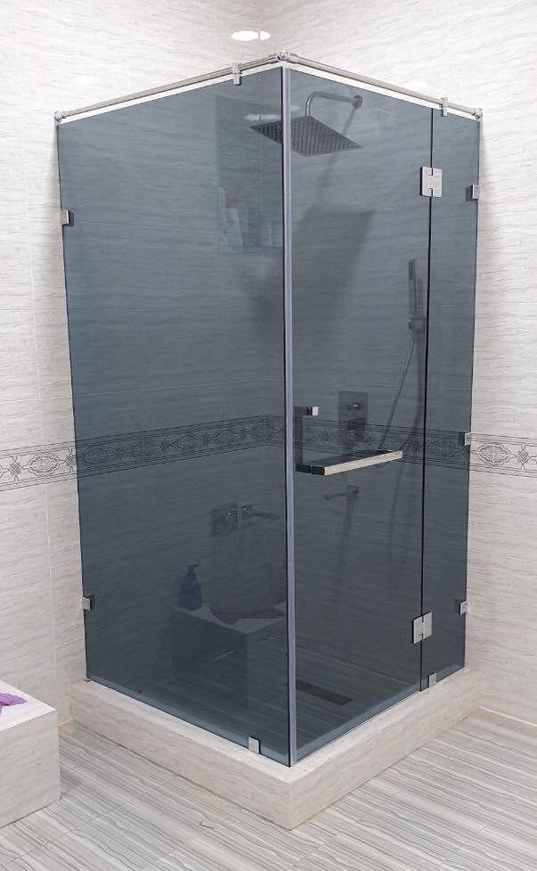 Box de chuveiro em vidro com painéis em tom cinza e ferragens cromadas, em um banheiro revestido com azulejos.