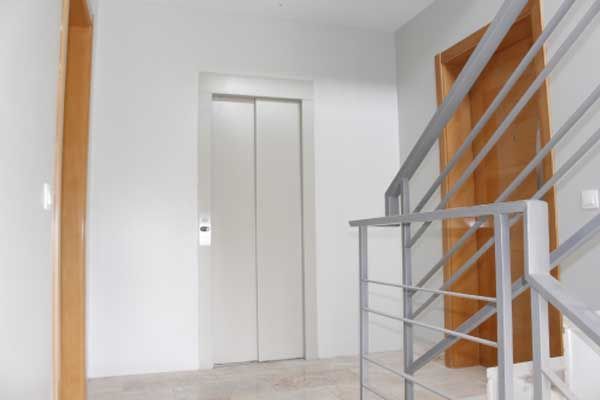 Portas de elevador brancas em um corredor entre uma moldura de porta de madeira e uma escada de metal.