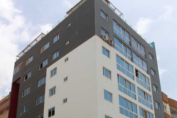 Prédio moderno de vários andares com fachada branca e cinza escuro e muitas janelas.