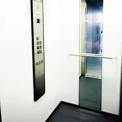 Mão de pessoa pressionando o botão para subir do elevador. O visor do elevador mostra zero.