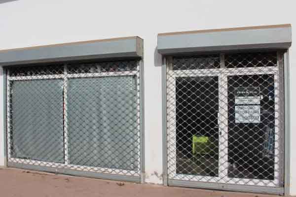 Fachada comercial com duas janelas, cada uma protegida por uma grade de segurança metálica.