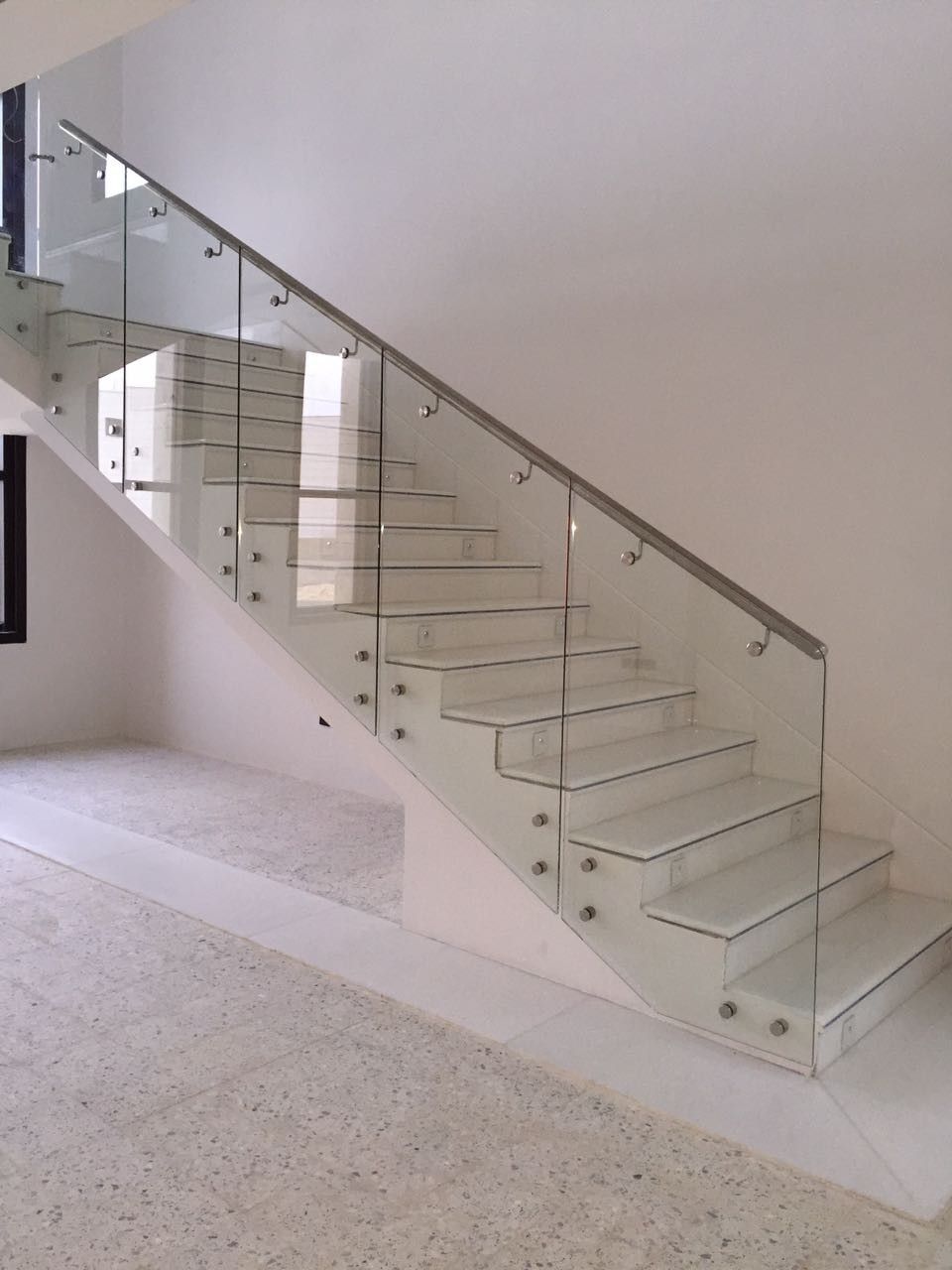 Escada moderna com painéis de vidro e corrimão de aço em um interior branco.