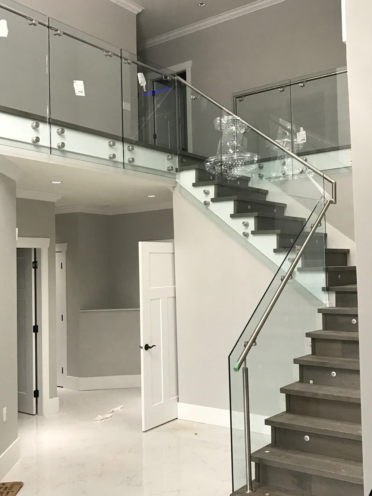 Escada com corrimão de vidro em uma casa moderna. Paredes cinza, degraus de madeira e interior iluminado.