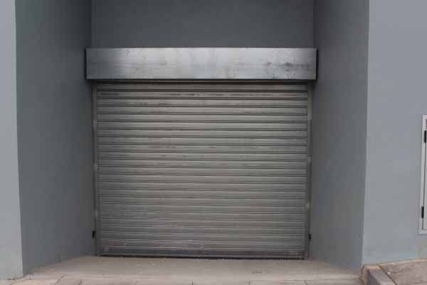 Porta de enrolar cinza fechada em uma parede cinza embutida.