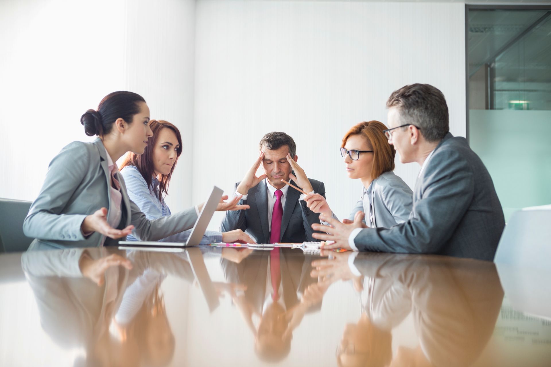 Réunion d'équipe autour d'une table de conférence. Les collaborateurs sont visiblement frustrés.