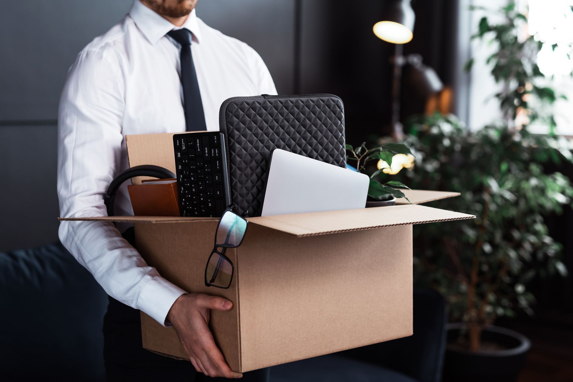 Un homme tient une boîte en carton rempli de fournitures de bureau.