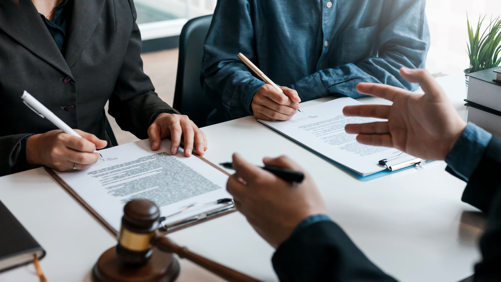 Des personnes signent des documents autour d'une table de conférence. Un maillet est placé au premier plan.