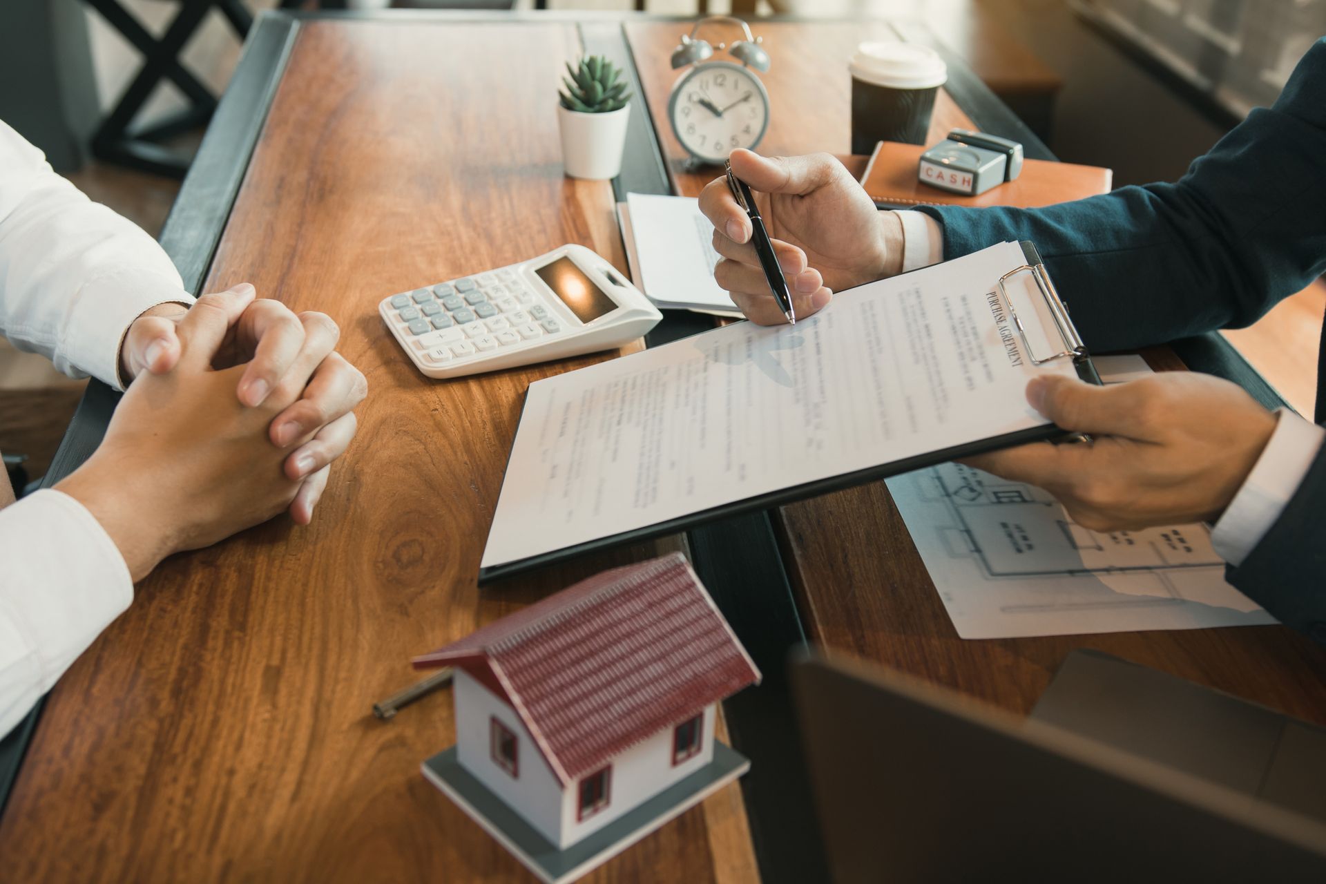 Un avocat montre un document à son client. Une calculatrice et une maquette de maison sont posées sur le bureau.