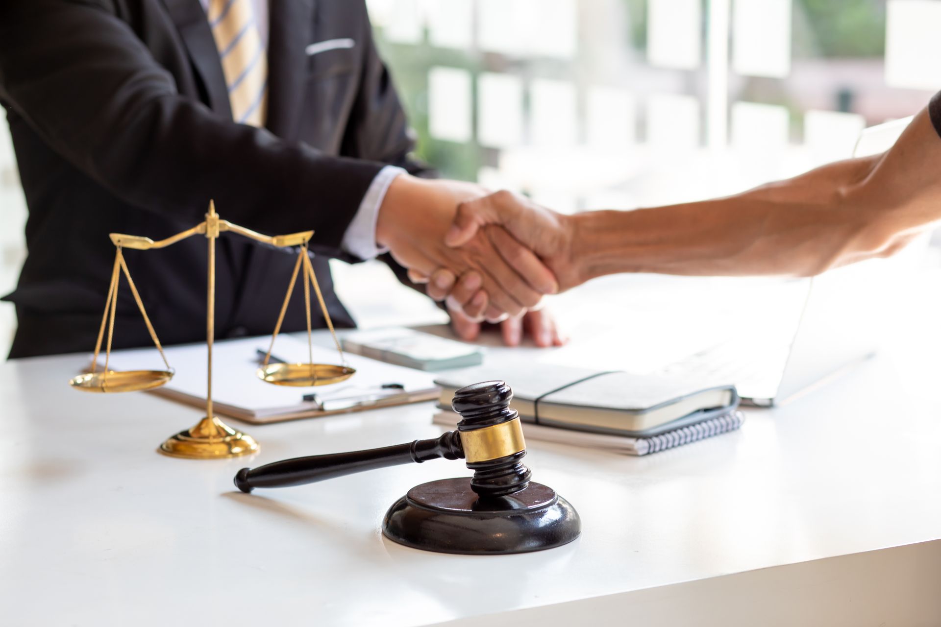 Deux hommes se serrent la main au-dessus d'un bureau où se trouvent une balance, un maillet et des documents.