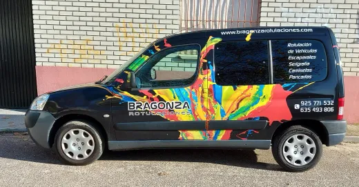 Coche hatchback negro con salpicaduras de pintura de colores arcoíris aparcado junto a una pared de ladrillos.