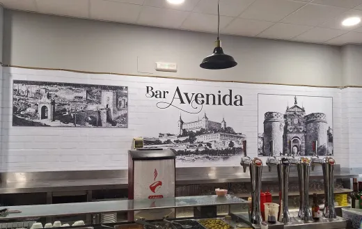 Mostrador del restaurante Bar Avenida con calentadores de comida y un mural en la pared con edificios de la ciudad y el nombre Bar Avenida.
