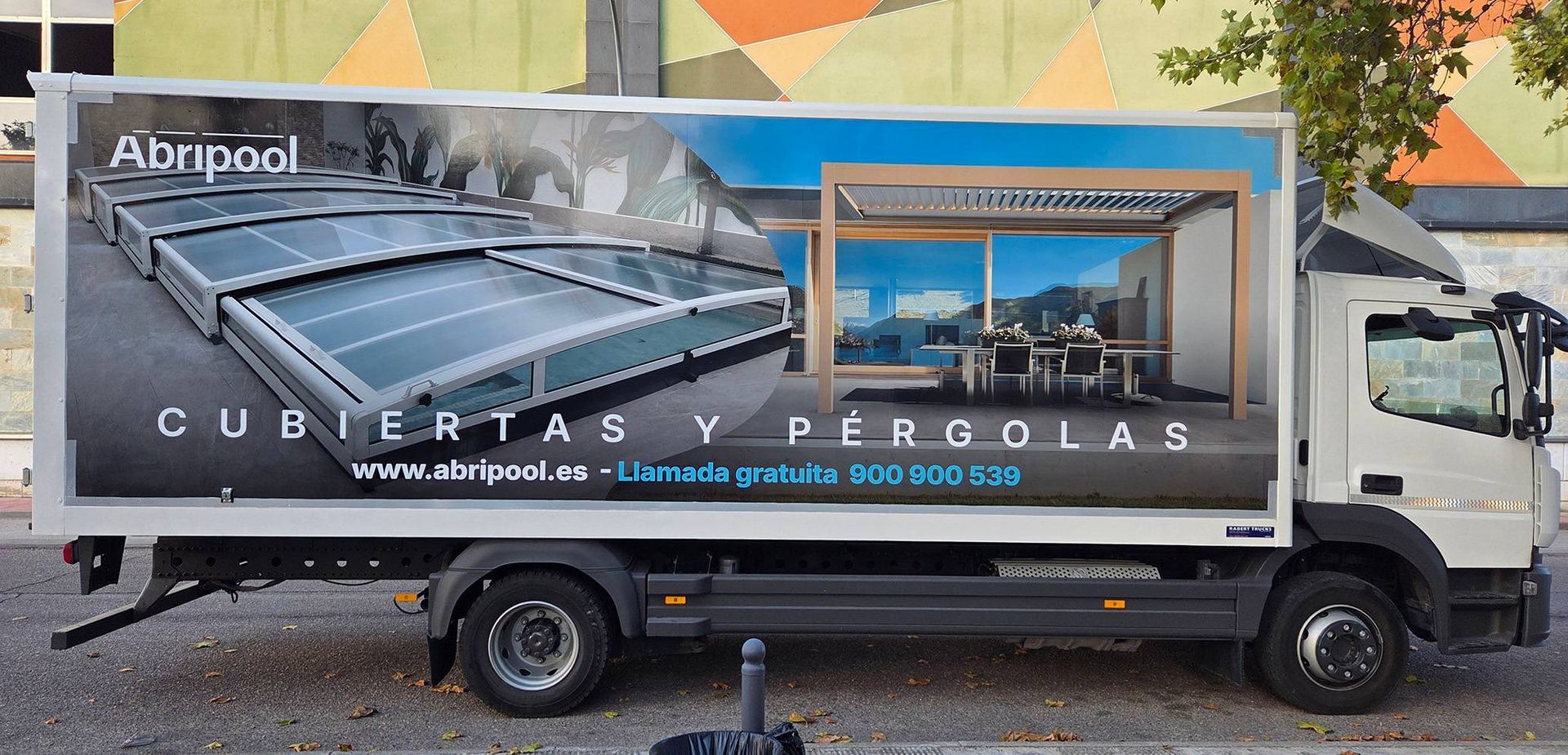 Camión comercial con pancarta publicitaria de cubiertas para piscinas y pérgolas en un estacionamiento.