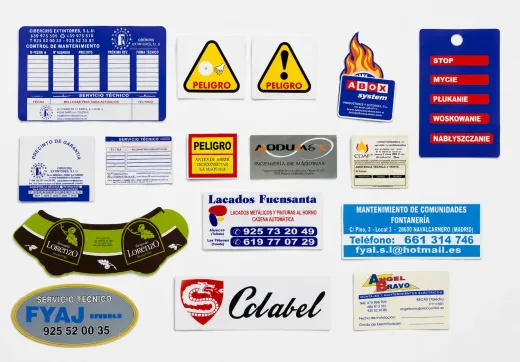 Varias etiquetas de advertencia y de marca, en su mayoría azules, amarillas, rojas y blancas, dispuestas en un collage sobre un fondo blanco.
