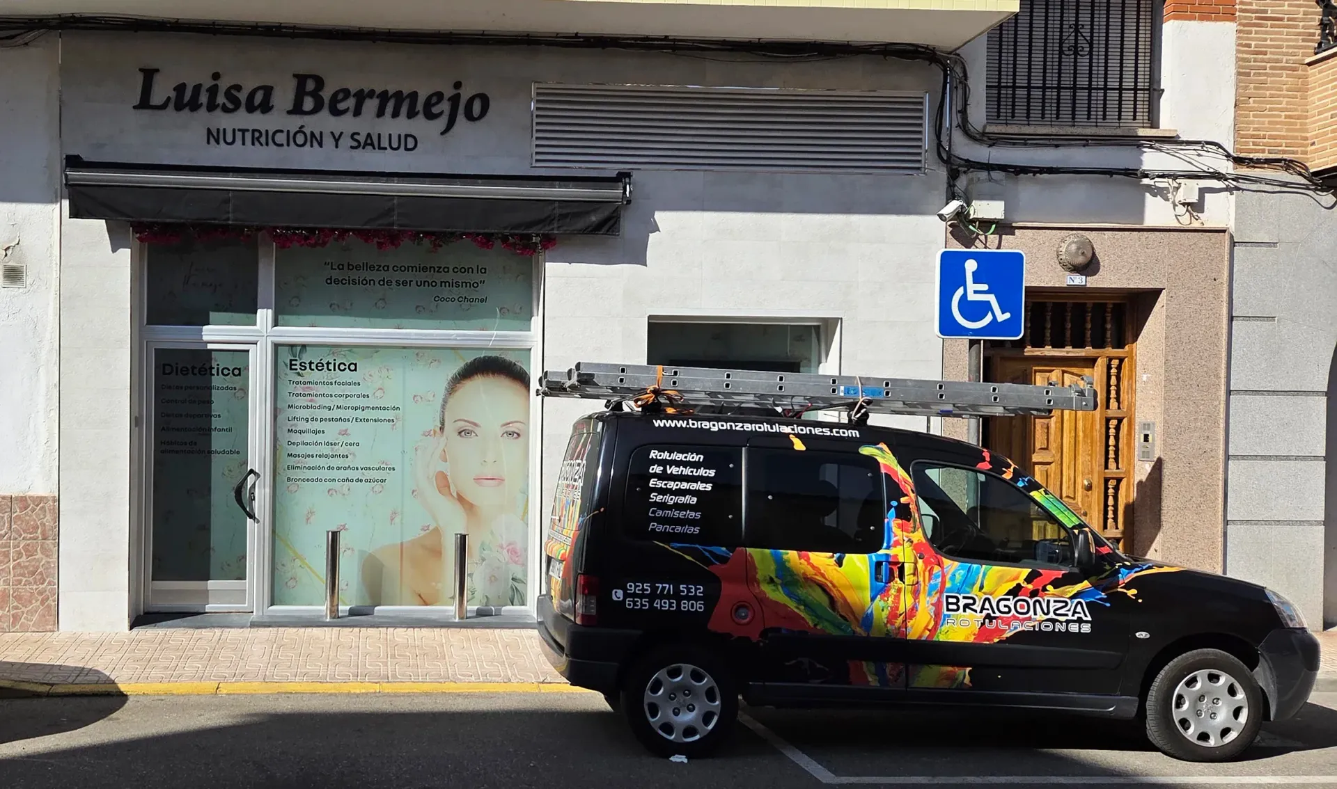 Un coche negro con un colorido mural aparcado frente al salón de Luisa Bermejo, junto a una señal de acceso para sillas de ruedas.