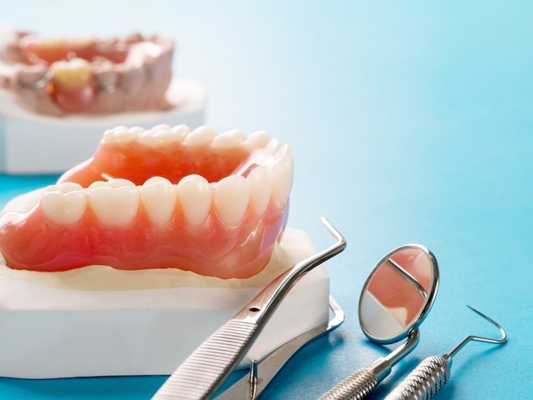 Un par de dentaduras postizas e instrumentos dentales sobre una superficie azul.