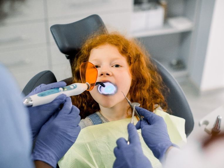 Una niña está sentada en una silla dental mientras un dentista le examina los dientes.