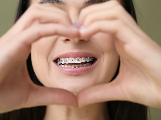 Una mujer con aparatos dentales está haciendo forma de corazón con sus manos.