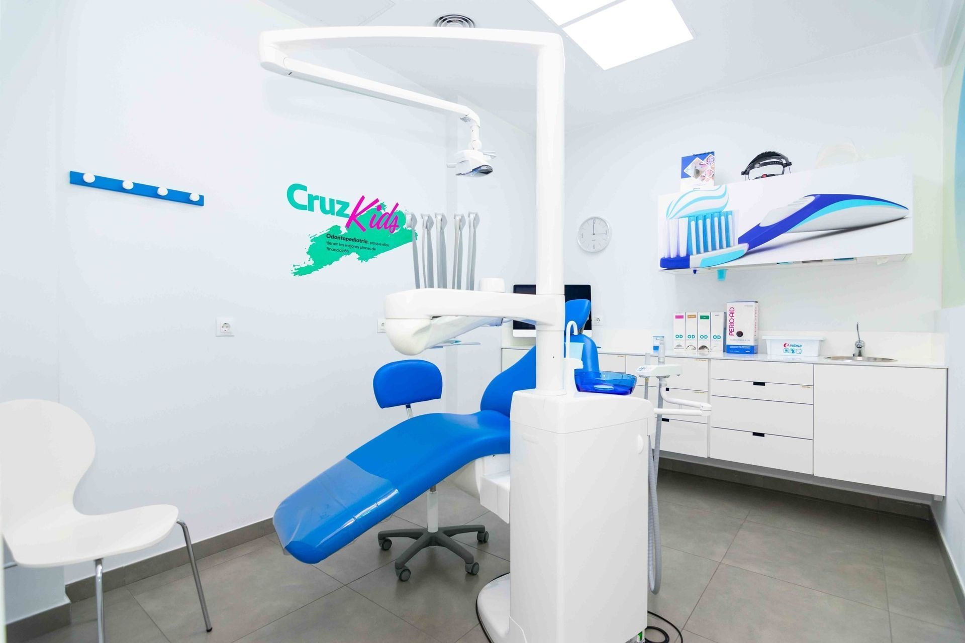 Un consultorio dental con un sillón dental azul y gabinetes blancos.