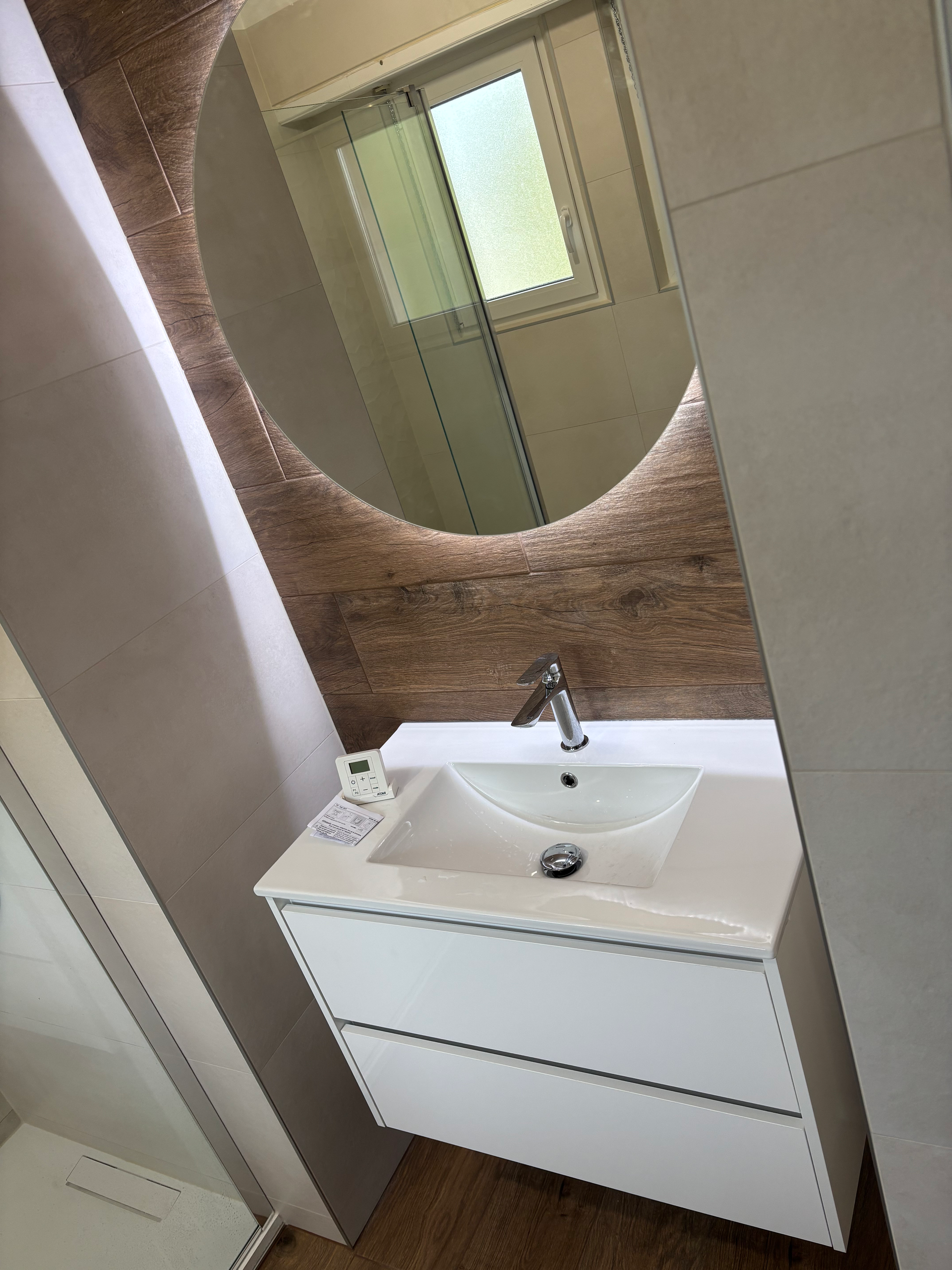 Meuble-lavabo moderne avec lavabo blanc, robinet chromé et miroir rond au-dessus d'un plan de travail.
