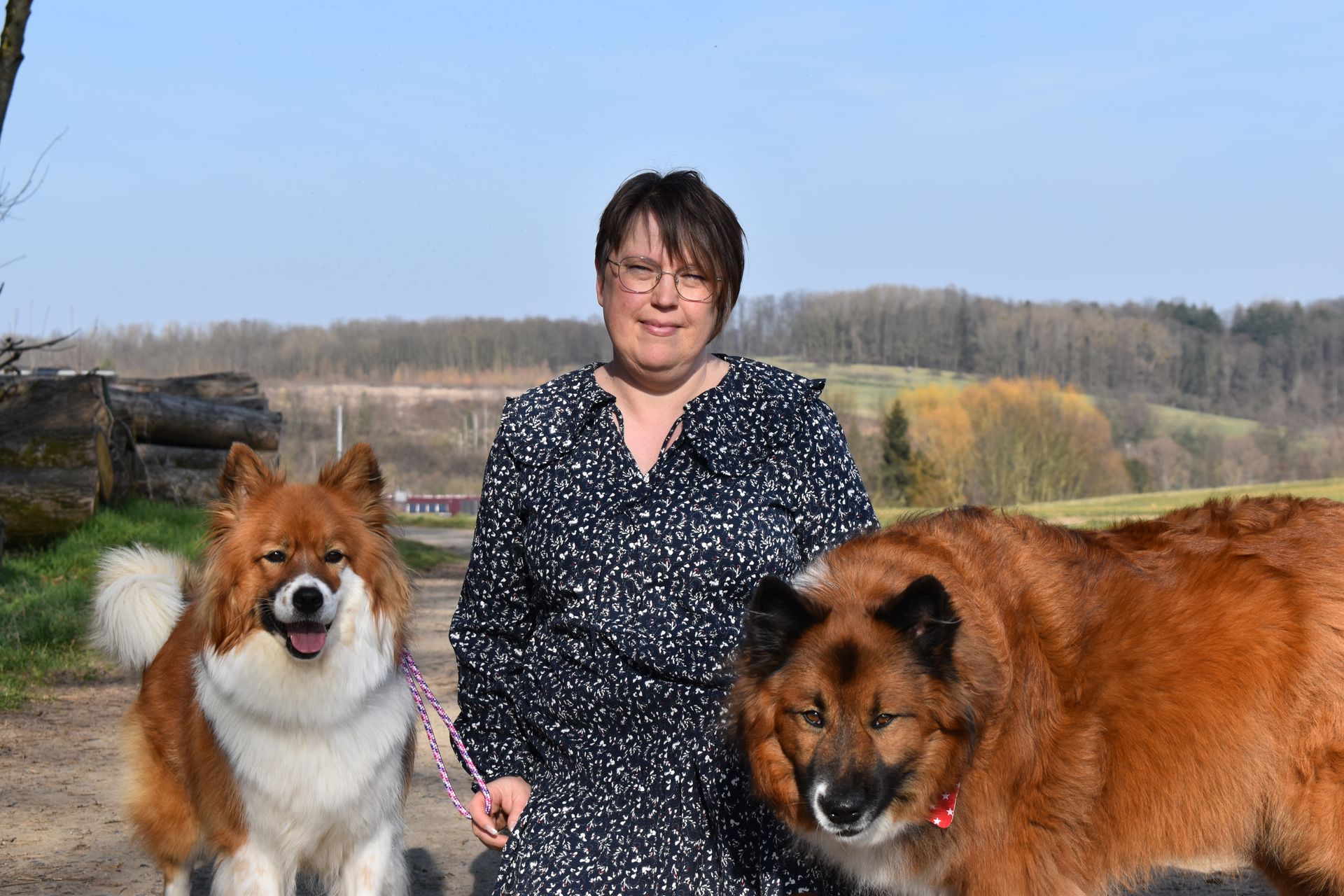 A woman is standing next to two dogs on a leash.