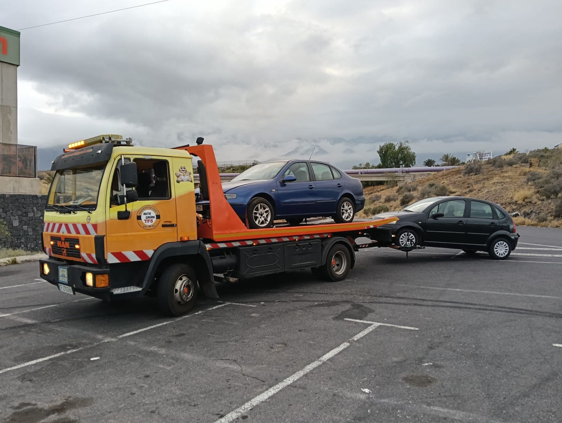 Un coche de carreras blanco en la rampa de una grúa en un aparcamiento con montañas al fondo.