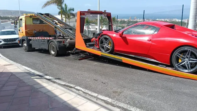Un coche deportivo rojo sobre una grúa junto a una carretera con vistas al océano.