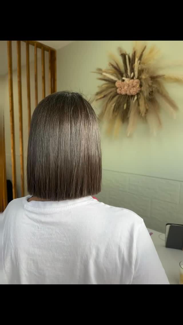 Persona con el pelo castaño hasta los hombros frente a una decoración de pared en una habitación, con una camisa blanca.