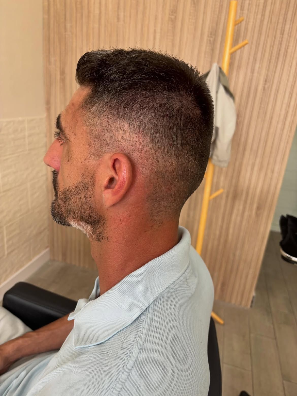 Perfil de un hombre con un corte degradado corto, sentado en una silla de peluquería.