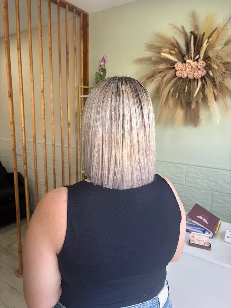 Una persona con un corte bob rubio y trenzado está de pie en una habitación, junto a una decoración de rayos de sol colgada