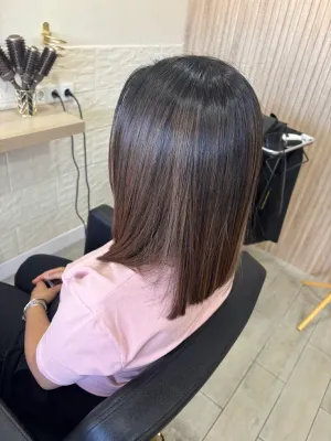 Persona con el pelo liso hasta los hombros, sentada en una silla de salón, vista desde atrás.