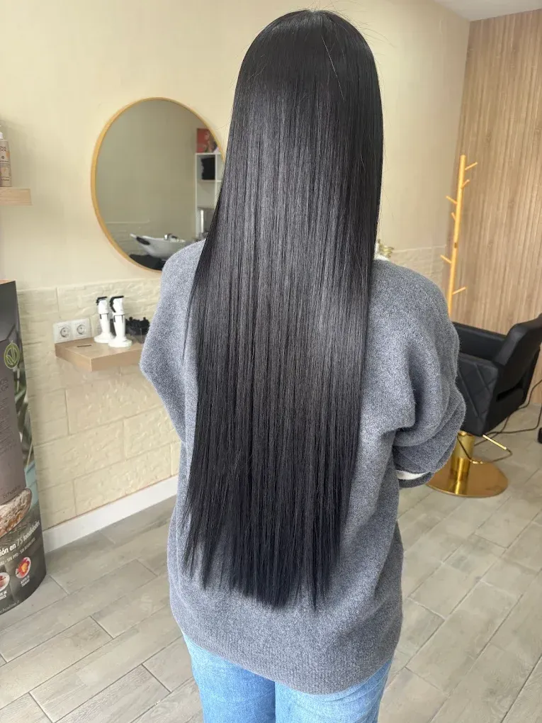 Persona de pelo largo y negro de pie en un salón, vista desde atrás, con un suéter gris y vaqueros.