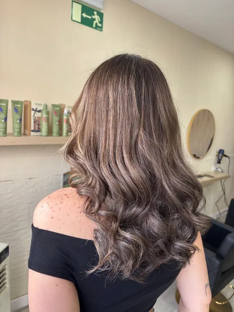 Mujer de cabello largo, castaño y ondulado, con una blusa negra de hombros descubiertos