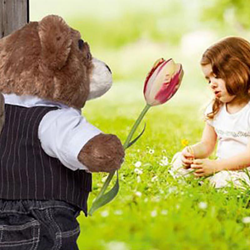 Ein Teddybär hält eine Tulpe vor einem kleinen Mädchen.