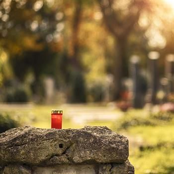 Auf einem Felsen auf einem Friedhof steht eine rote Kerze.